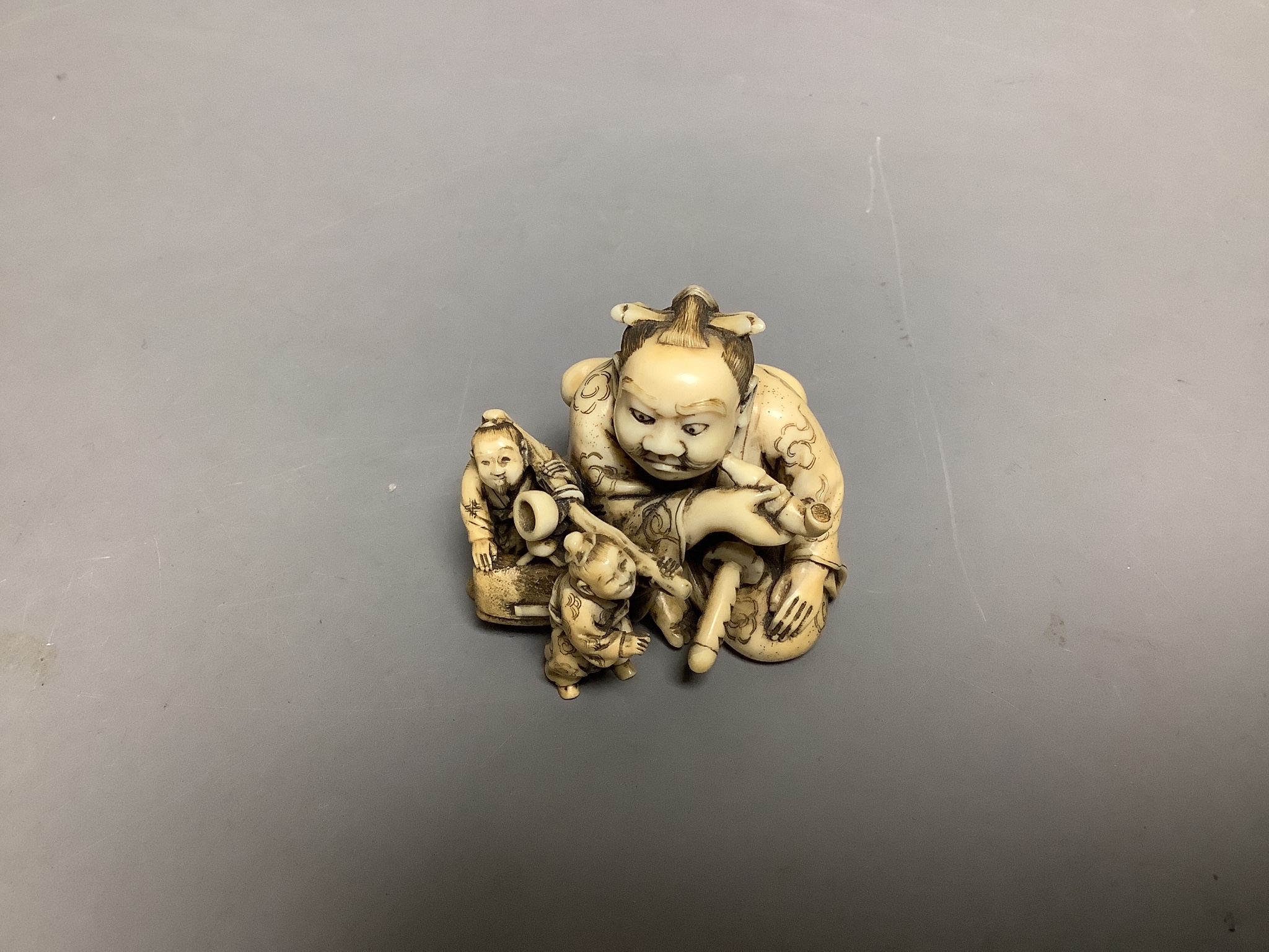 A Japanese ivory netsuke of two miniature men carrying a Samurai's tobacco pouch, Meiji period, signed